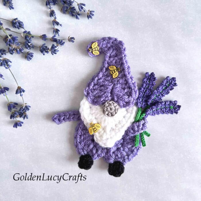 Crocheted gnome with lavender flowers in his hand.