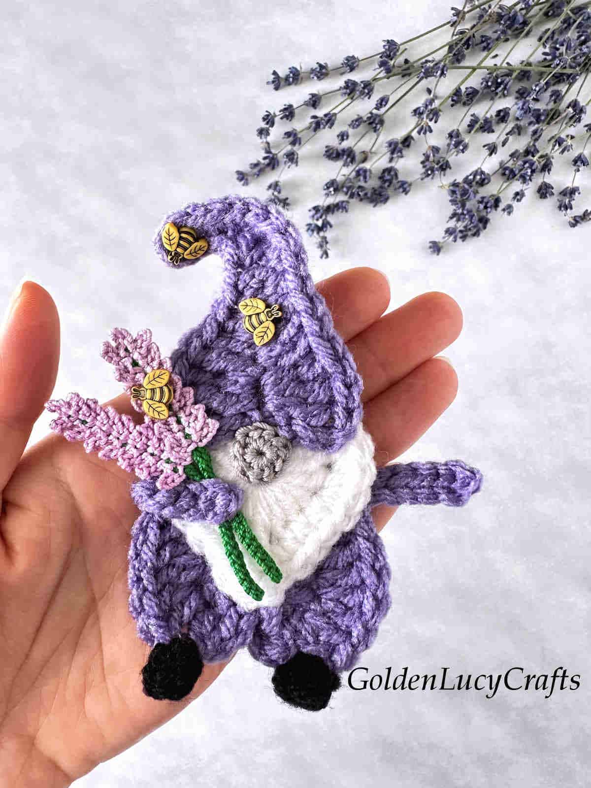 Crochet lavender gnome in the palm of a hand.