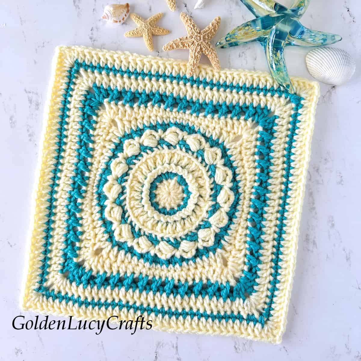 Crochet square block in cream and aqua colors, star fish and sea shell in the background.