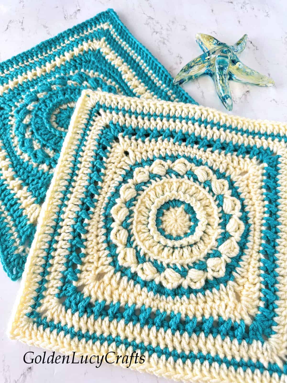 Two crocheted square motifs made in cream and aqua colors, glass star fish in the background.