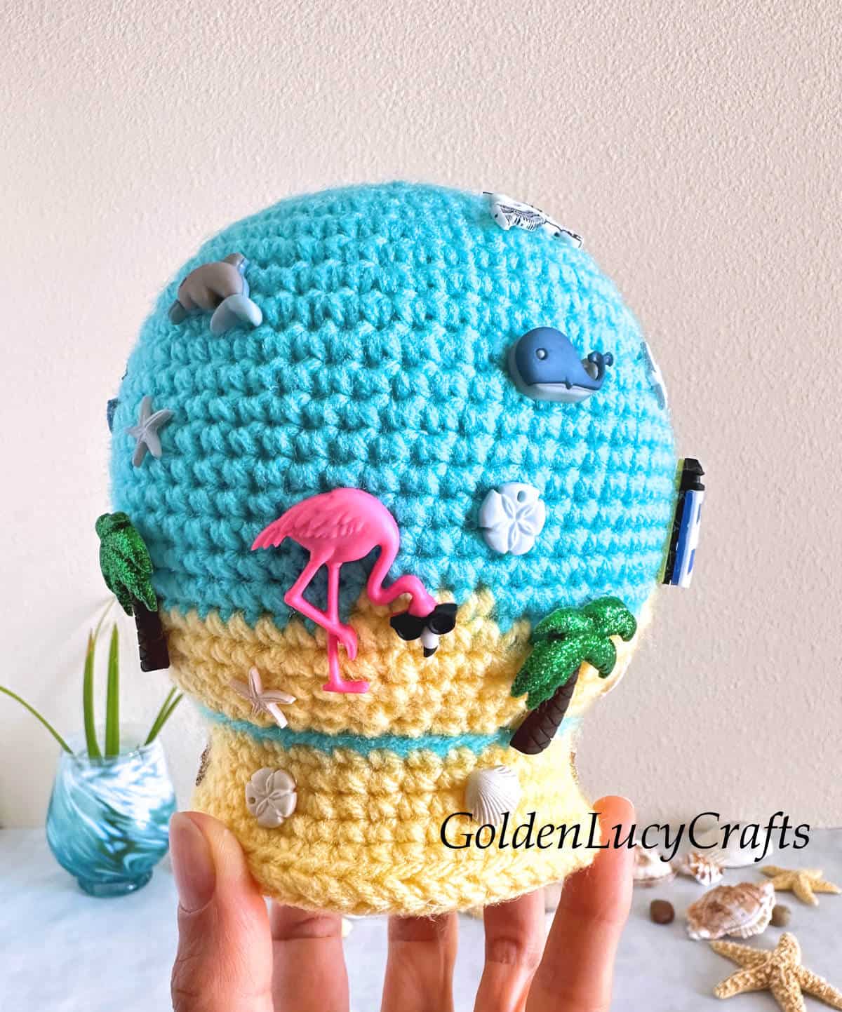 Crocheted summer themed snow globe held by fingertips.