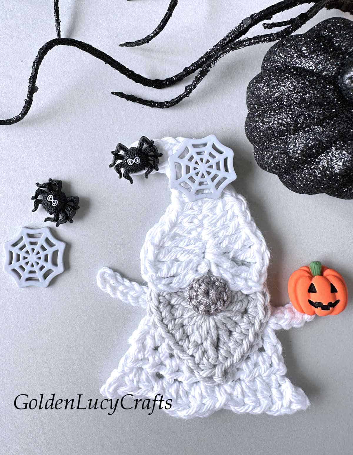 Crochet ghost gnome applique with spider and spider web on his cap and pumpkin in his hand.