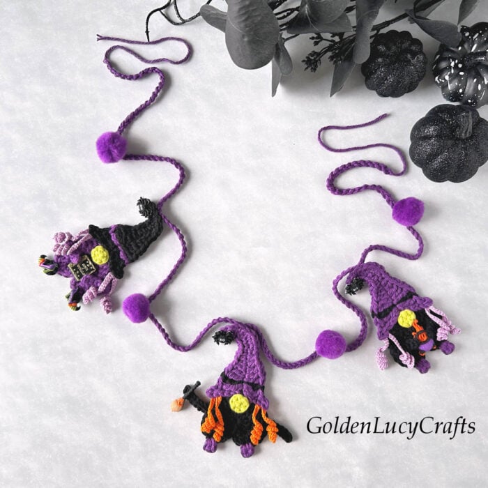 Crochet Halloween garland with witch gnomes and purple pom-poms.