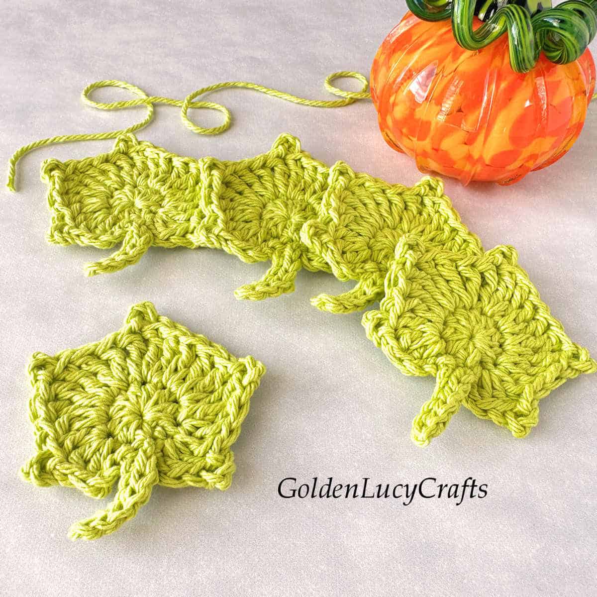 Five crocheted pumpkin leaves laying next to the glass pumpkin.