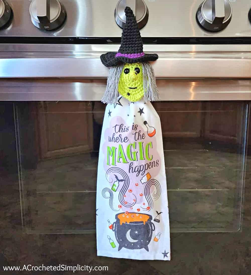 Kitchen towel with crocheted witch face hanging on the oven door.