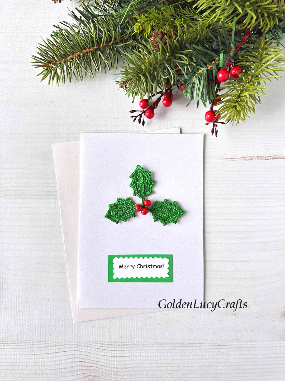 White card with crocheted holly berry applique and a note saying Merry Christmas.