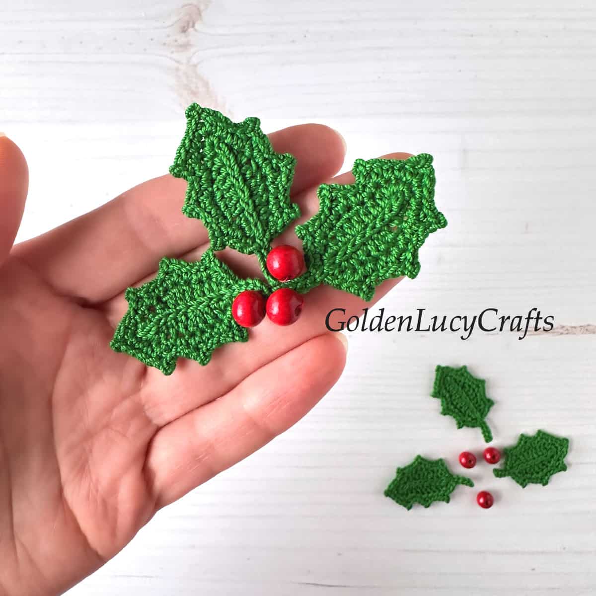 Crochet holly applique in the palm of a hand.
