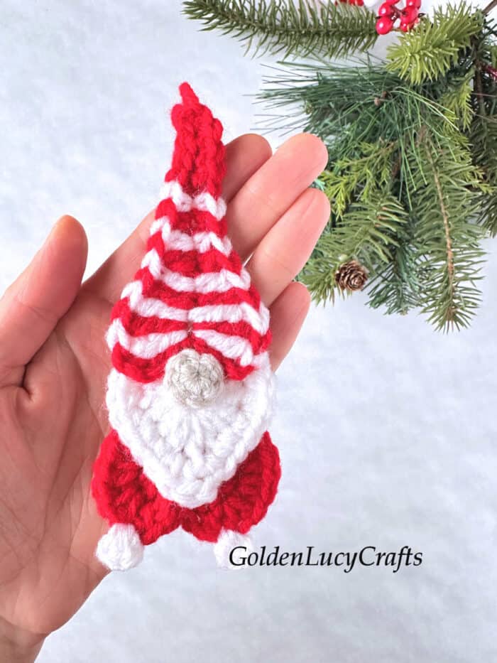 Crochet candy cane gnome in the palm of a hand.
