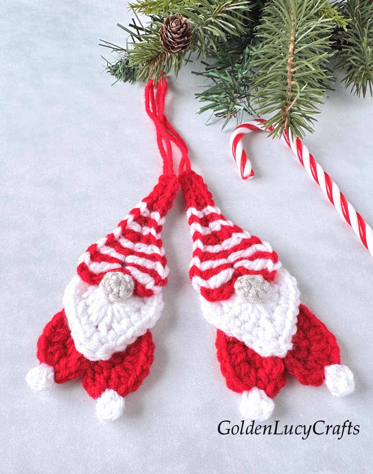 Two crocheted gnomes and candy cane next to them.