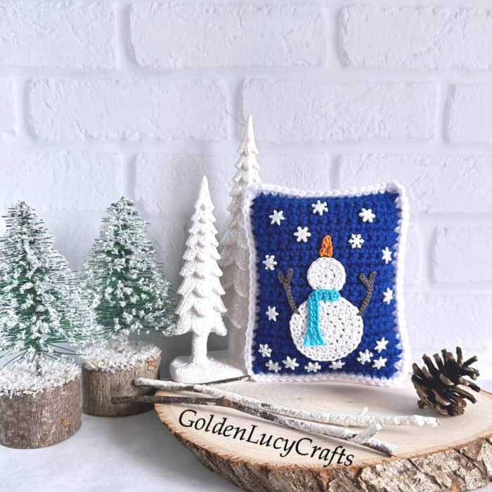 Crocheted decorative mini pillow with snowman catching snowflakes on it.