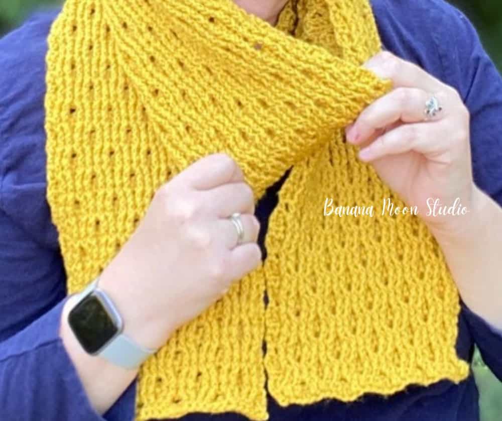 Crocheted yellow scarf wrapped around model's neck.