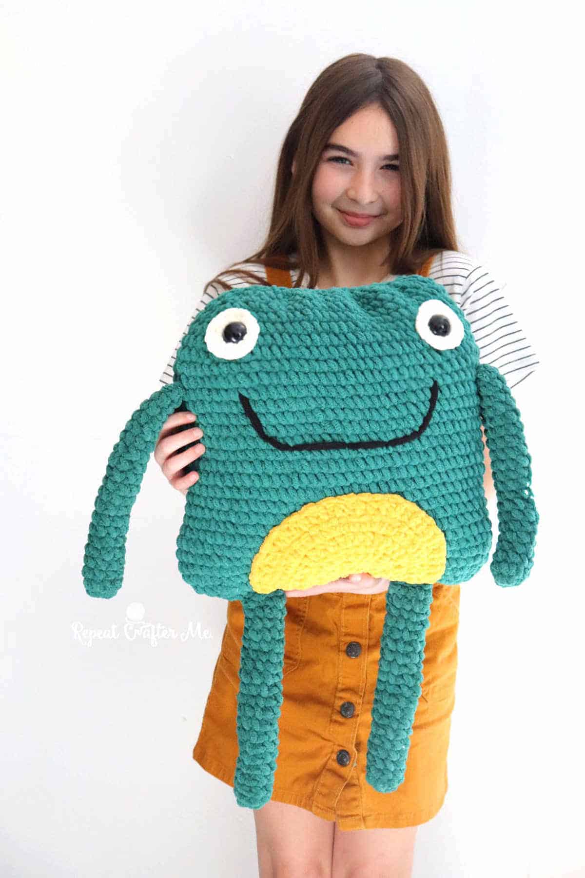Girl holding crocheted frog pillow.