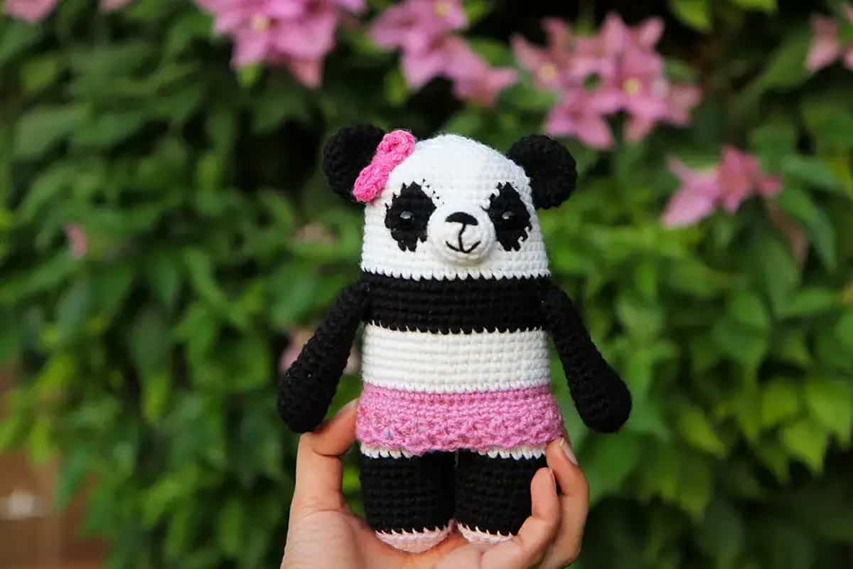 Crocheted panda amigurumi held by hand.