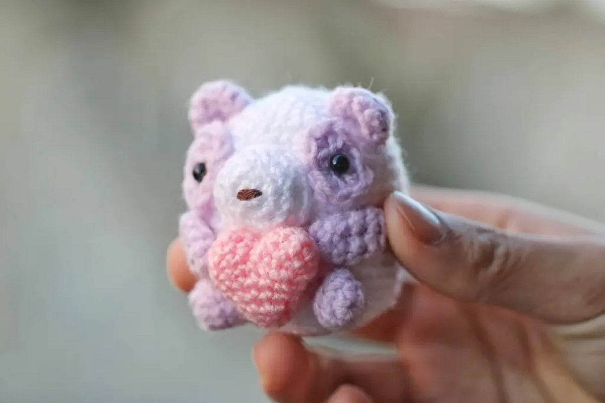 Crocheted small panda with heart held by hand.