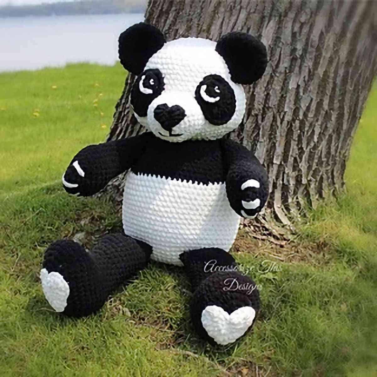 Crocheted large panda toy sitting next to tree.