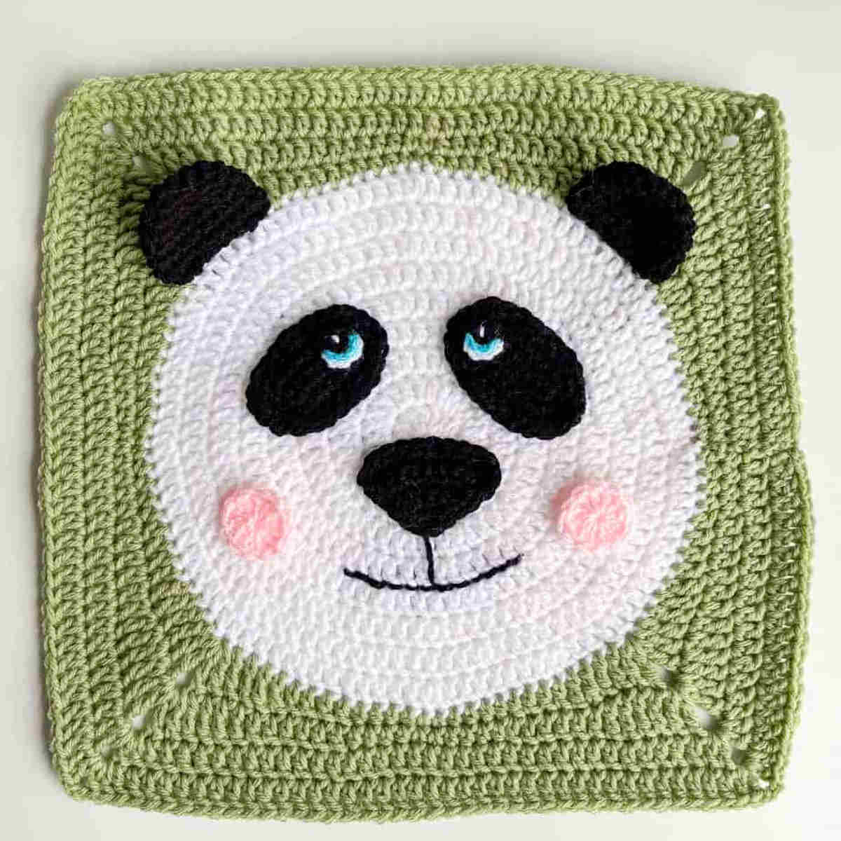 Crocheted green square with panda face in the center.
