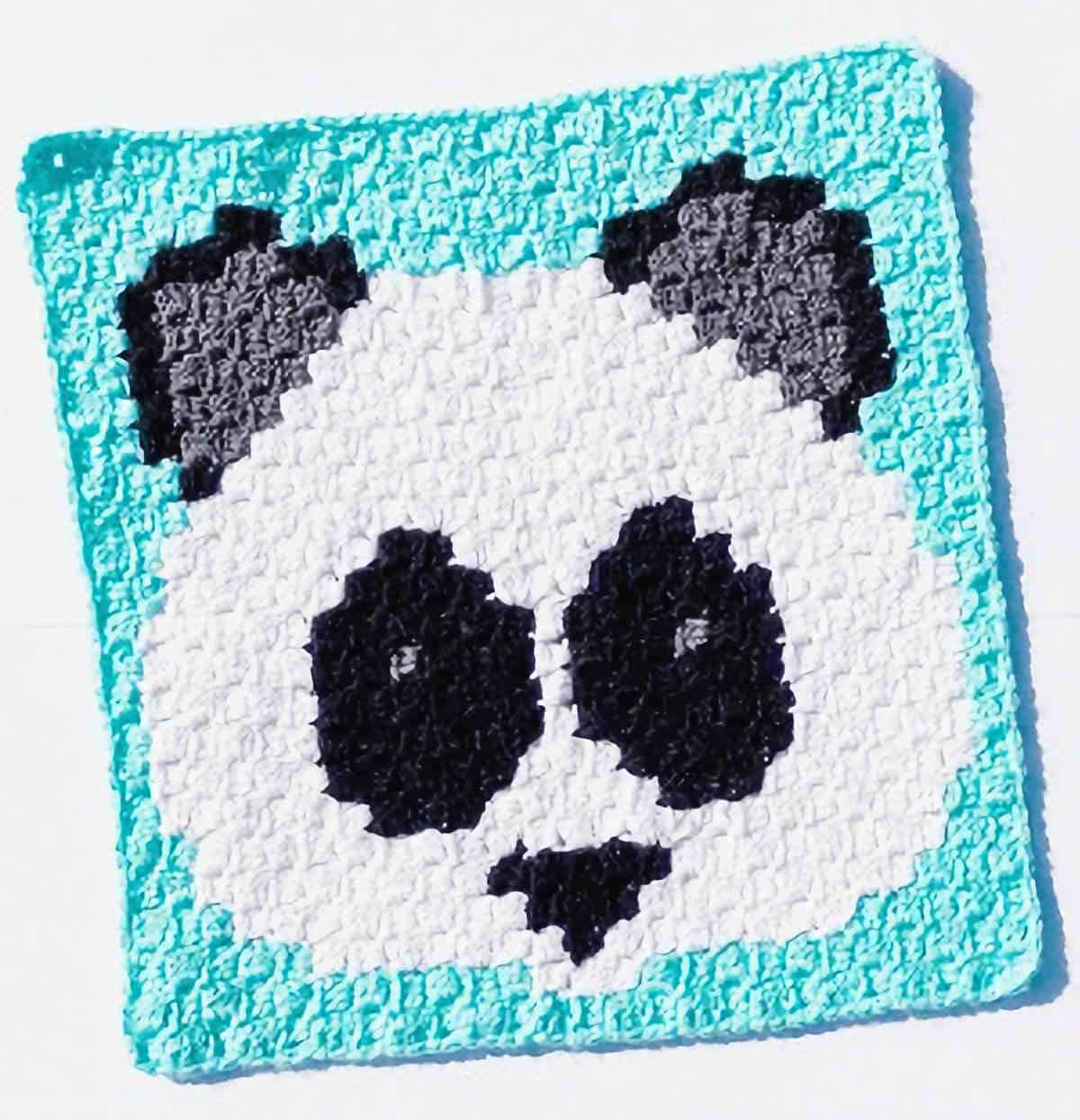 Crocheted blue square with panda face on it.