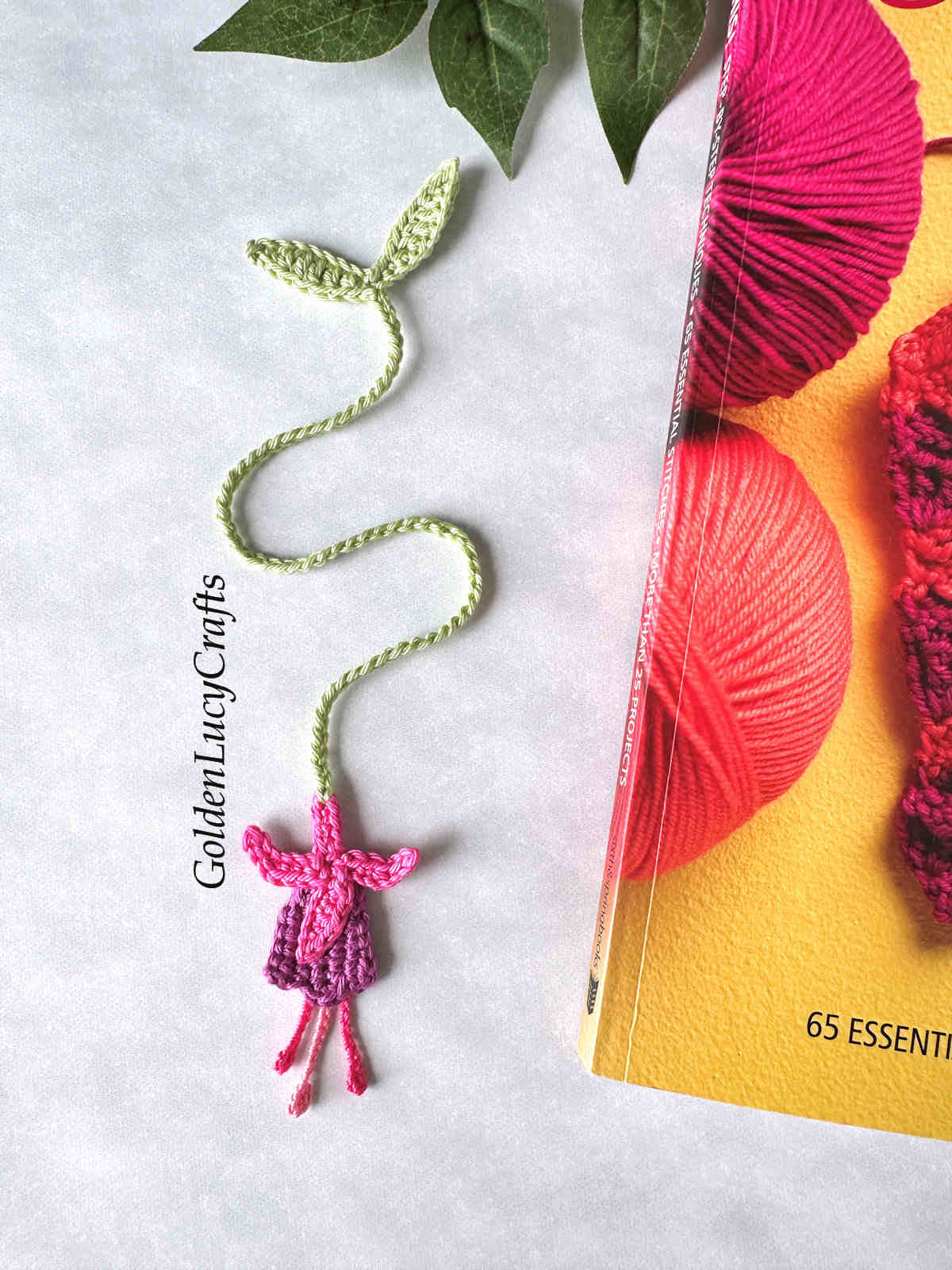 Crocheted fuchsia bookmark laying next to the book.