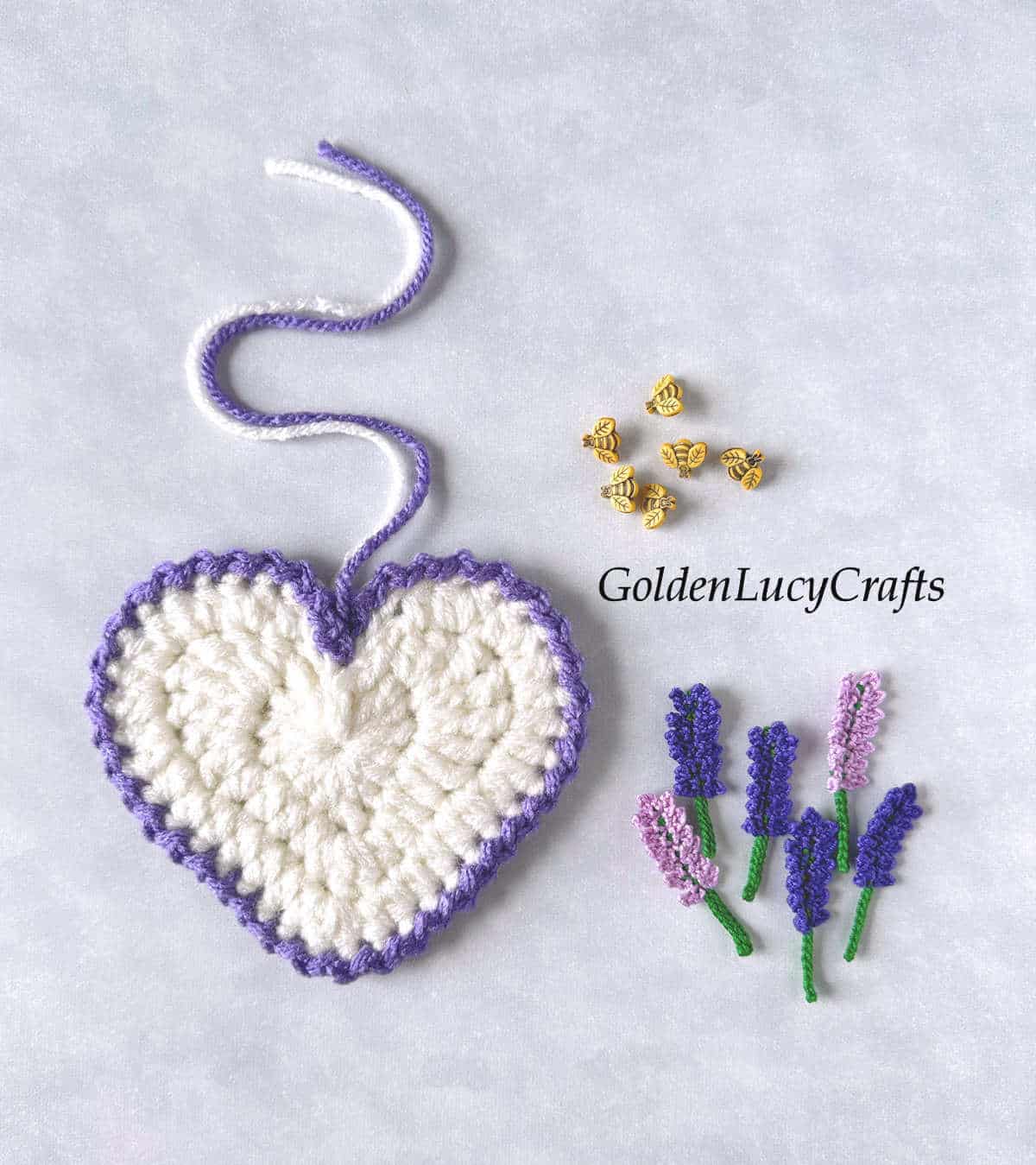 Crocheted heart in white color with purple edging, crochet lavender appliques and decorative bee buttons.