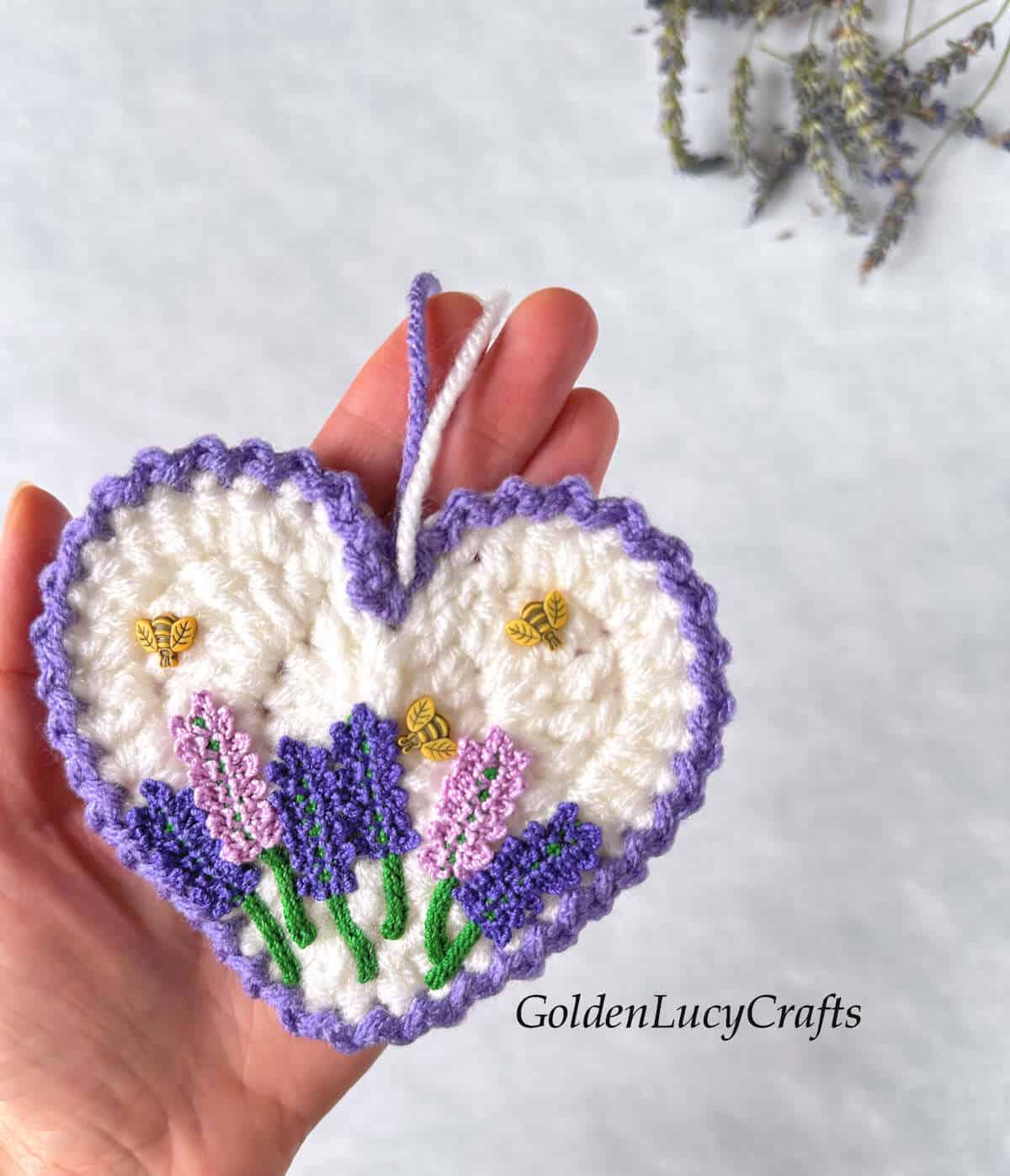 Crochet lavender heart in the palm of a hand.