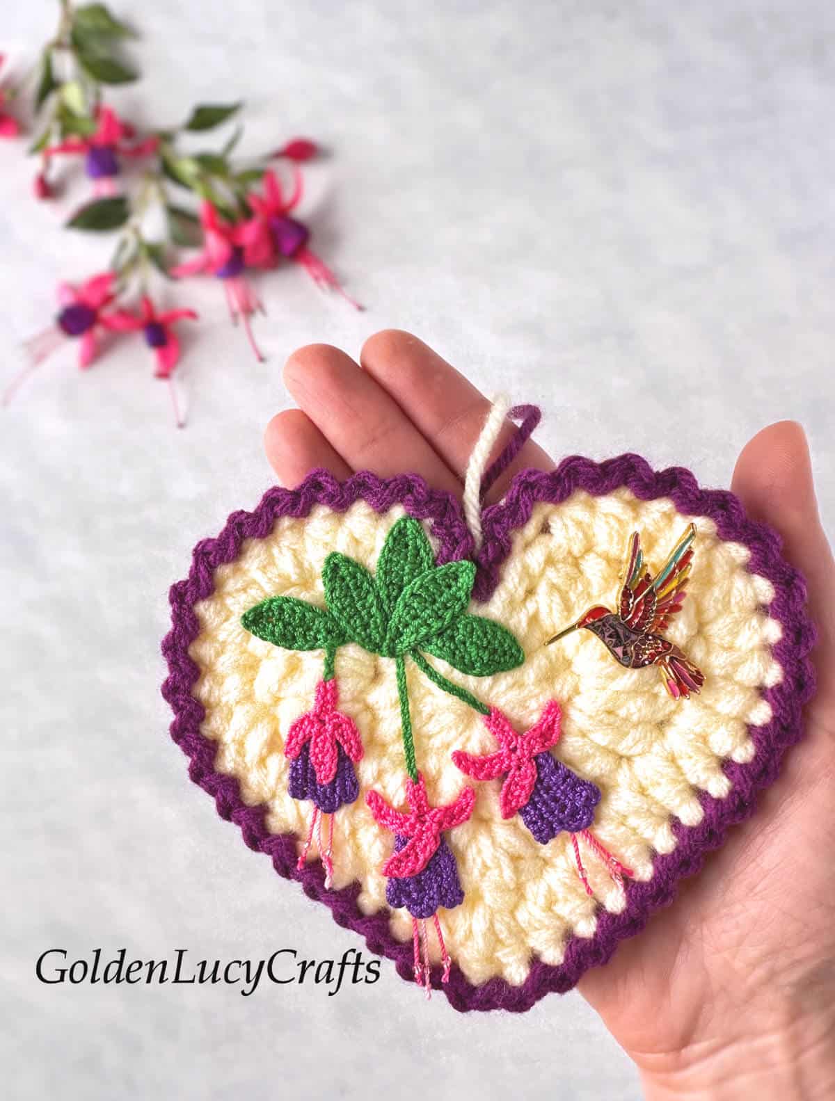 Crochet fuchsia heart ornament in the palm of a hand.