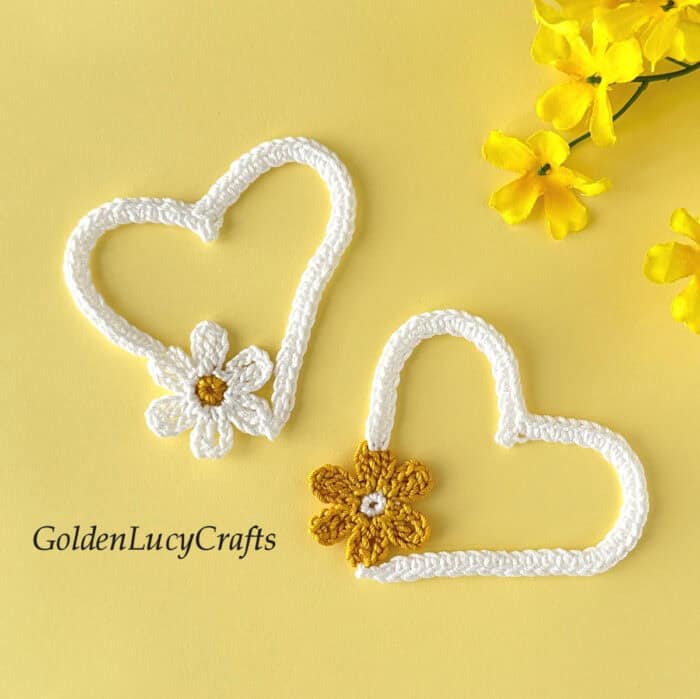 Two crocheted white hearts with flowers on a yellow background.