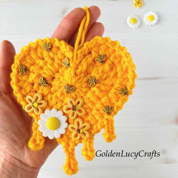 Crochet honey heart ornament in the palm of a hand.