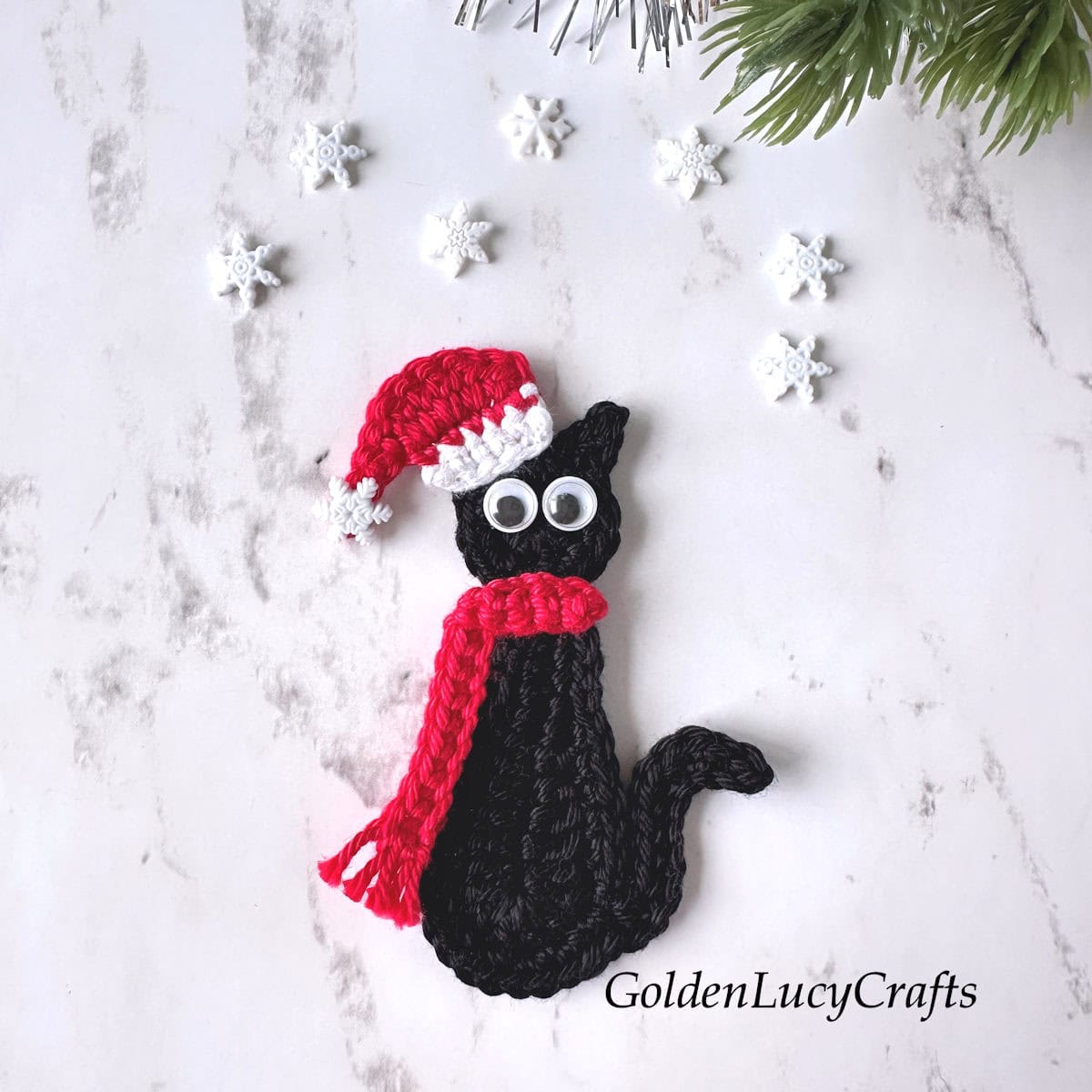 Crochet applique black cat with googly eyes dressed in a Santa hat and red scarf.