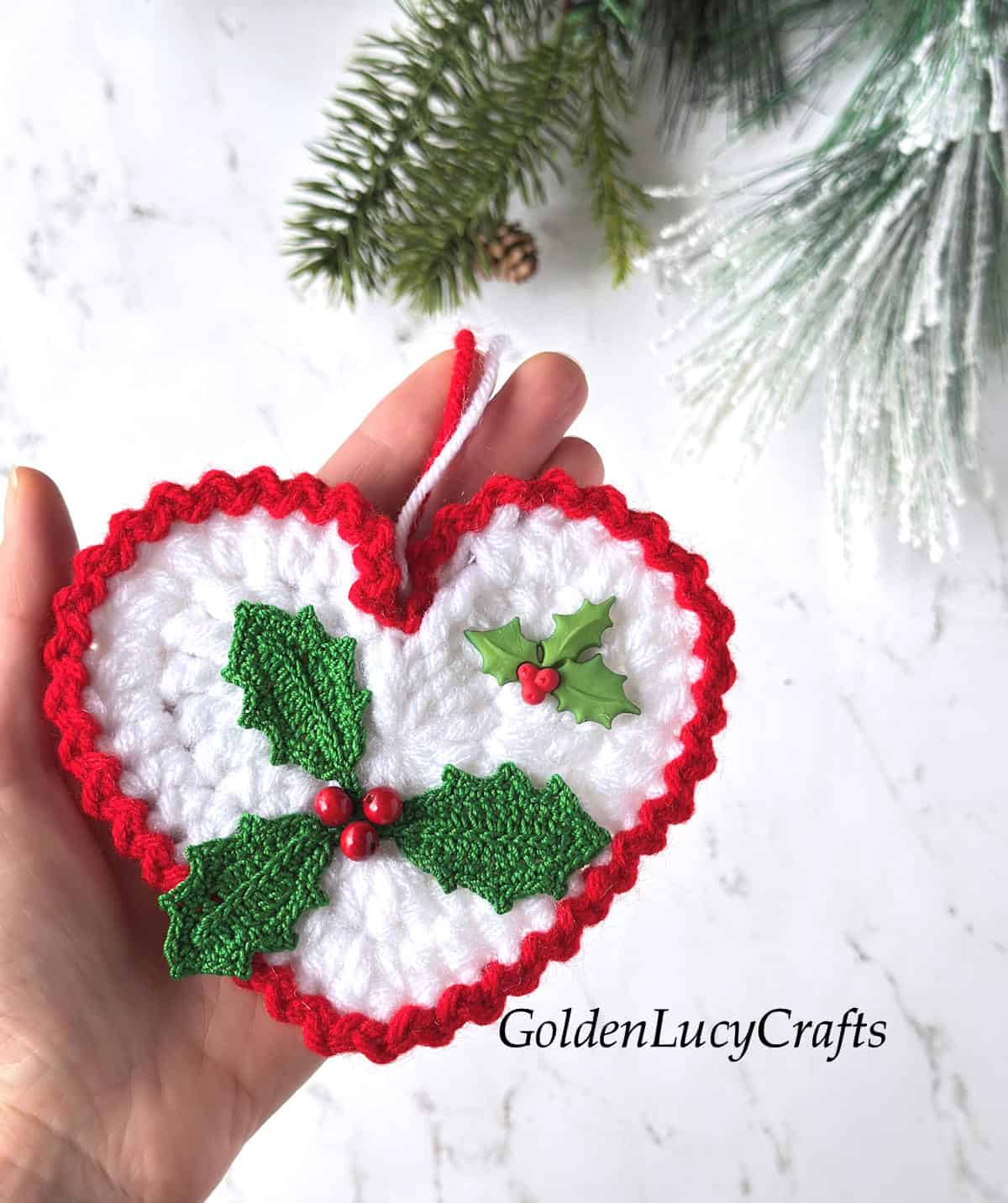 Crochet holly ornament in the palm of a hand.