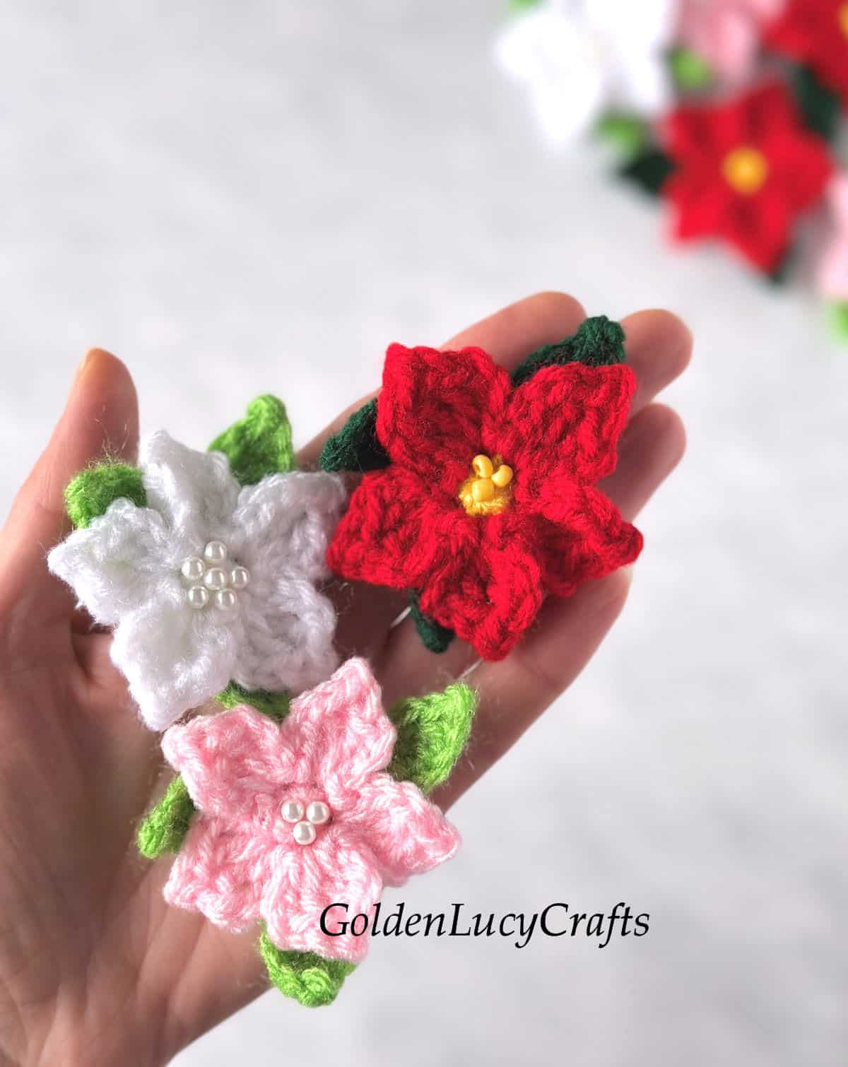 Three crocheted poinsettia flowers in the palm of a hand.