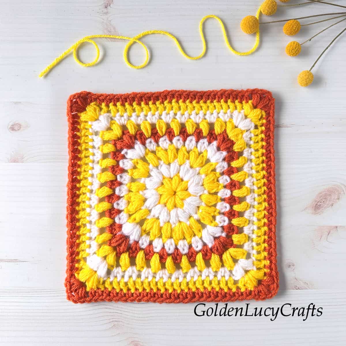 Crocheted square made using puff stitches and half double crochet stitches in yellow, white, and orange colors.