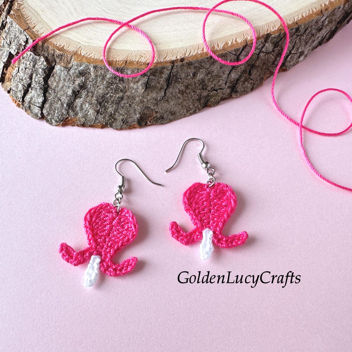 Crocheted bleeding heart flower earrings next to a wood slice.