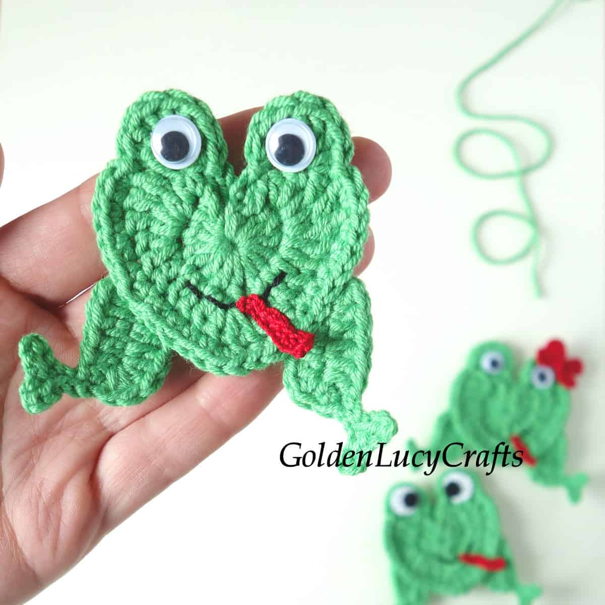 Crochet green frog applique in the palm of a hand.