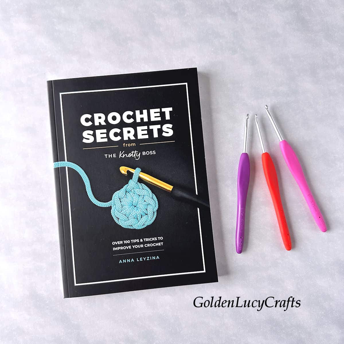 The book titled "Crochet Secrets" is placed beside three crochet hooks.