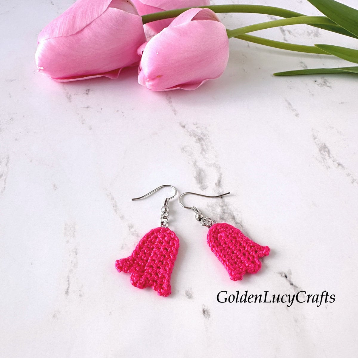 Crocheted bright pink tulip earrings, soft pink real tulips in the background.
