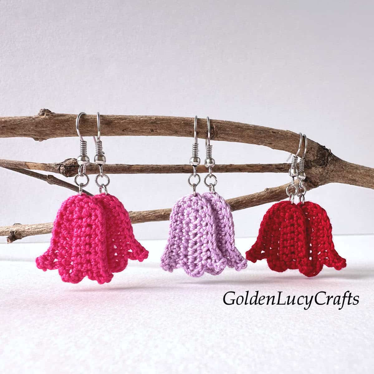 Three pairs of crocheted tulip earrings are displayed on a branch.