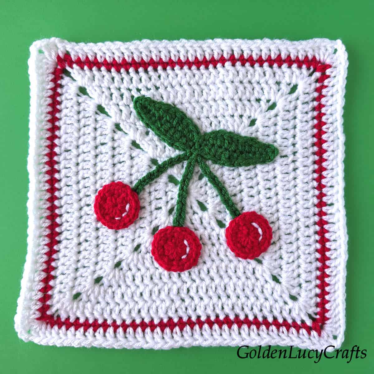 Crocheted white squre with cherry applique on it.