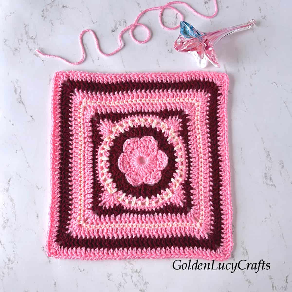 Crocheted square made in pink, dark red and cream colors.