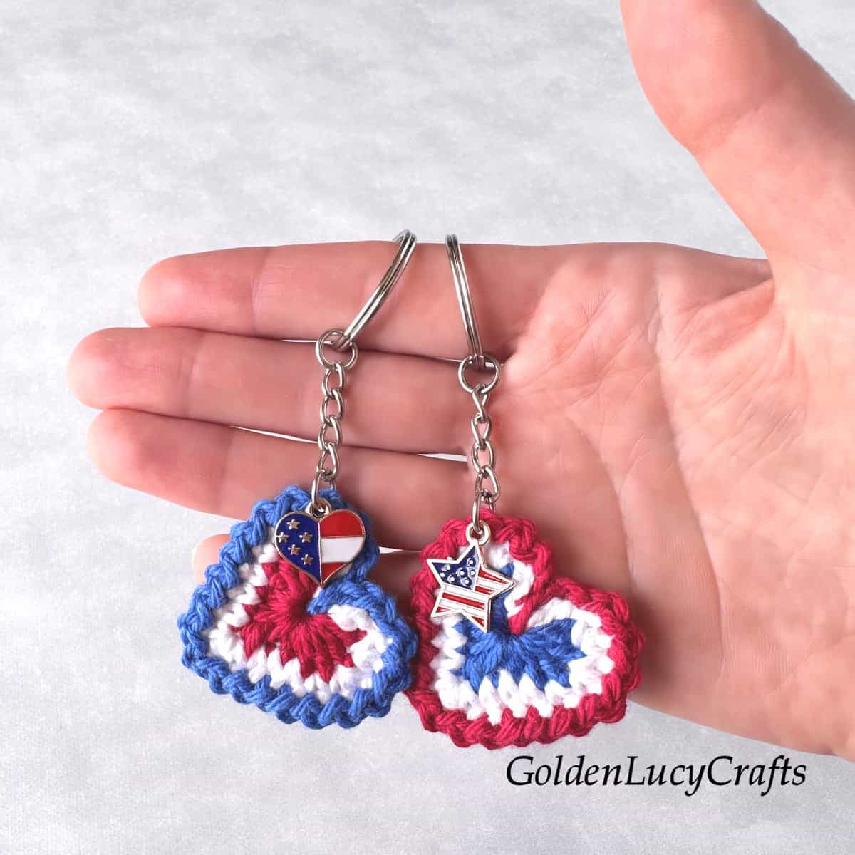 Two crocheted patriotic heart keychains in the palm of a hand.