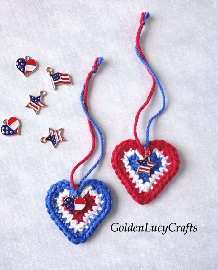 Two crocheted American flag hearts, charms lying next to them.