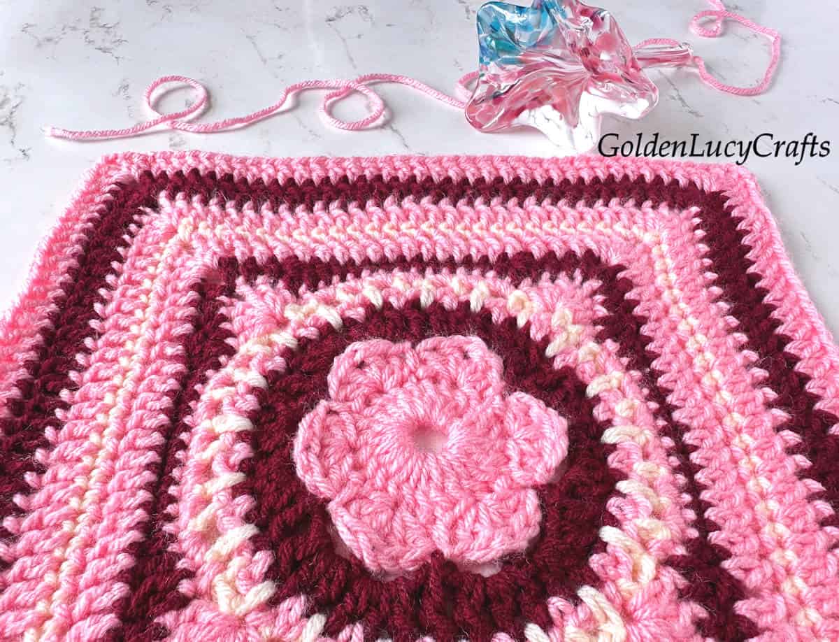 Crocheted square block made in pink, dark red and cream colors, close up picture.