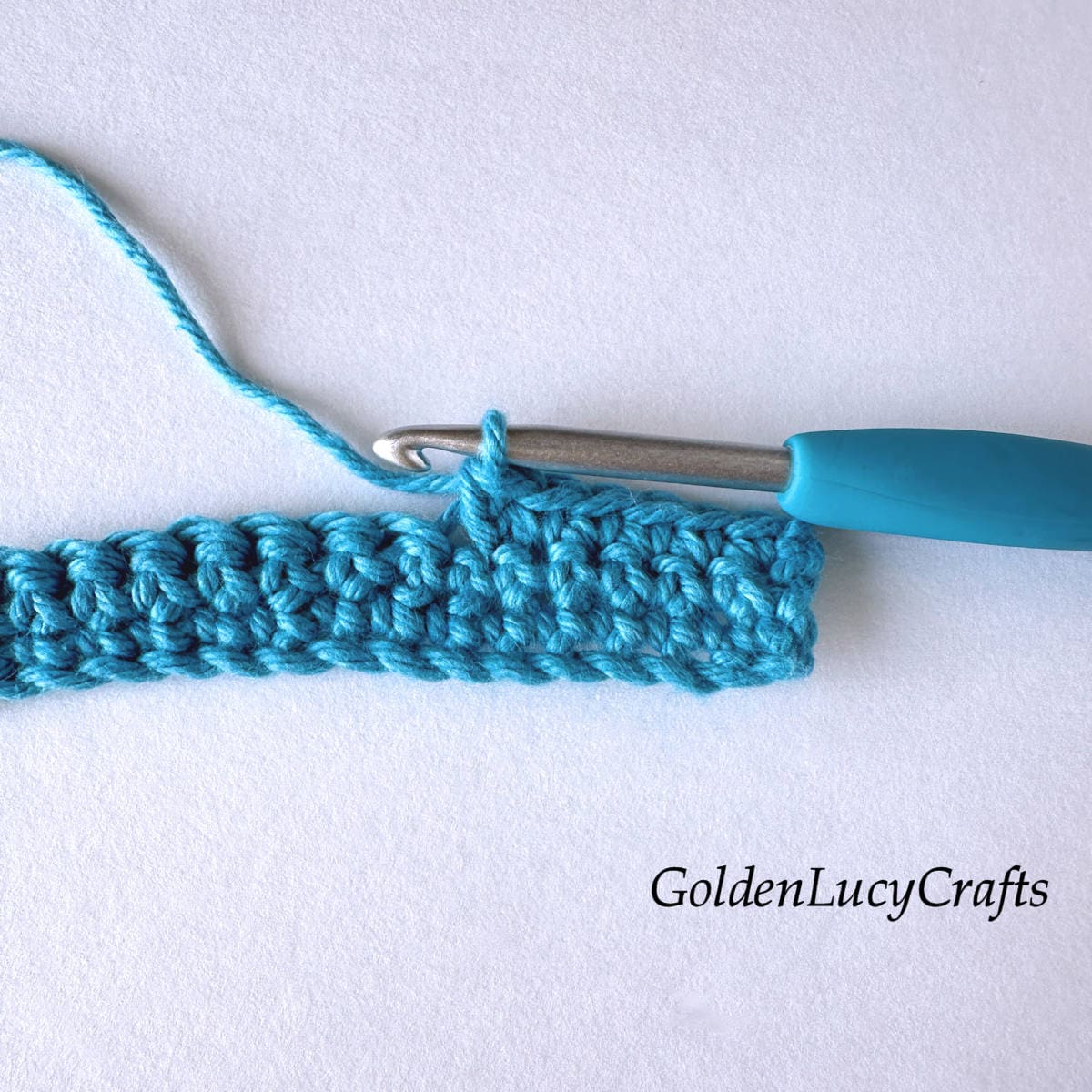 Crocheted sample in teal color and crochet hook.