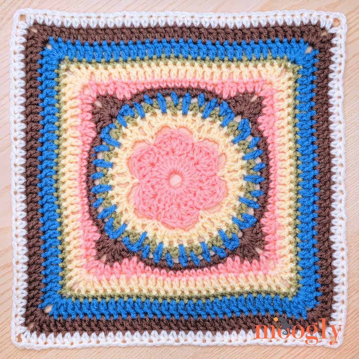 Crocheted square made in various colors with a flower in the center.