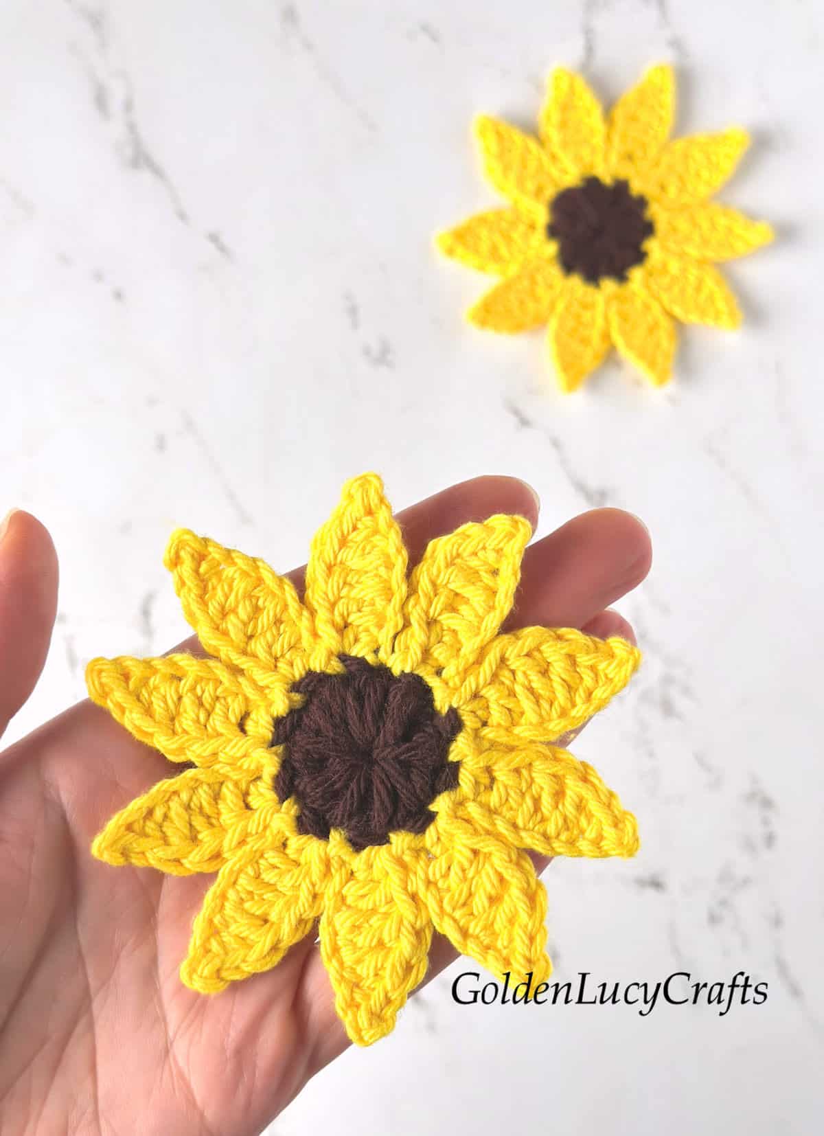Crocheted sunflower in the palm of a hand.