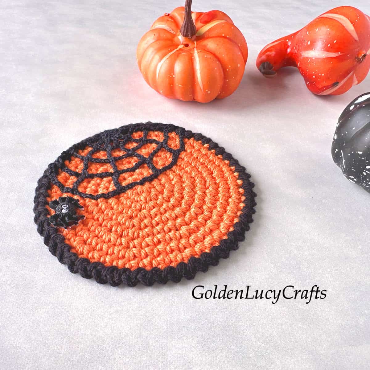 Crocheted Halloween coaster in orange, featuring a spider web with a small spider, along with small pumpkins.
