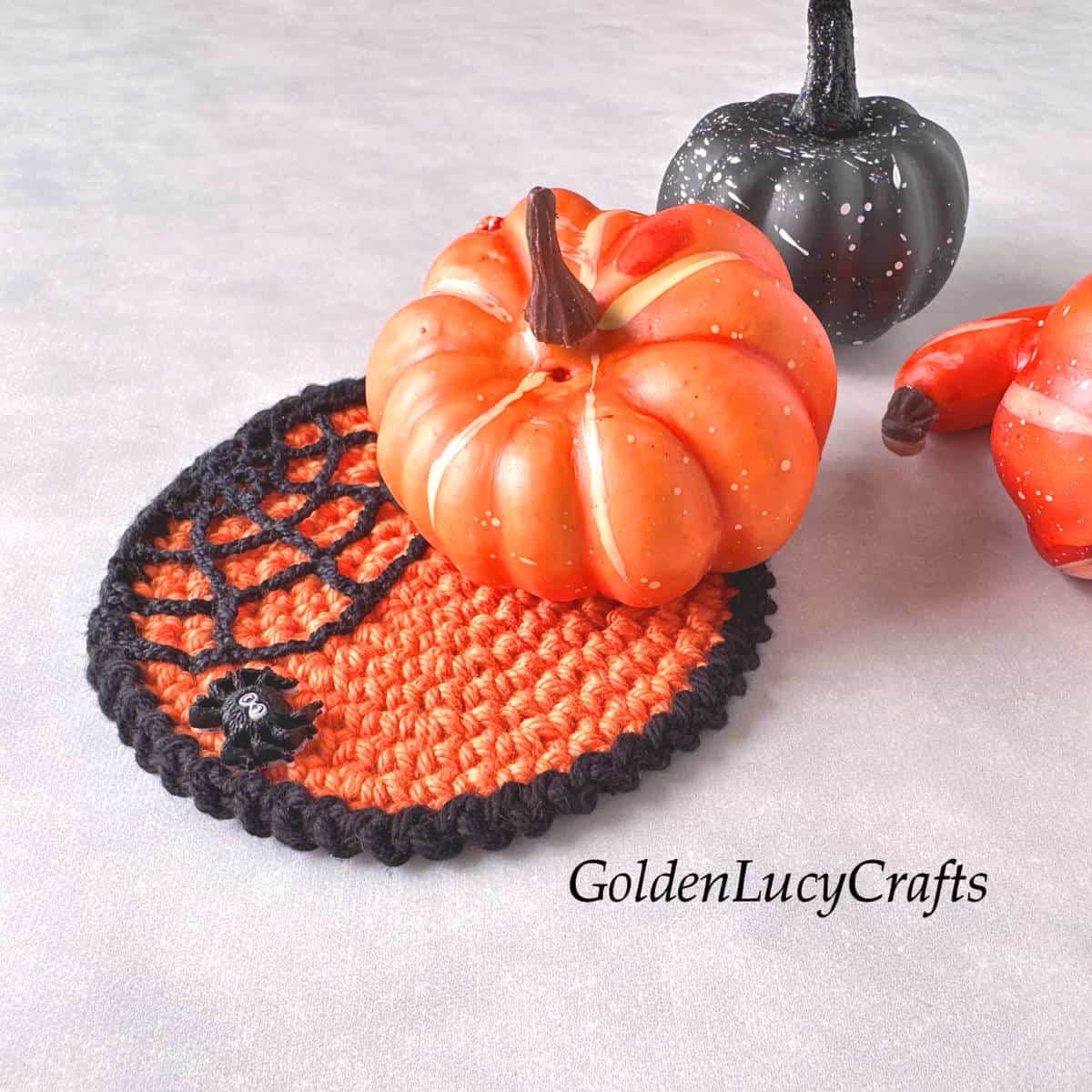 Crocheted Halloween coaster in orange, featuring a spider web with a small spider, along with orange and black pumpkins.