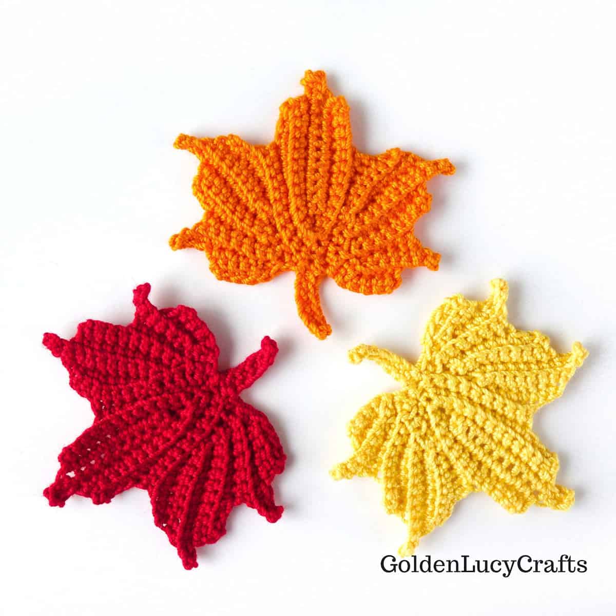 Three crocheted maple leaves in red, yellow, and orange.