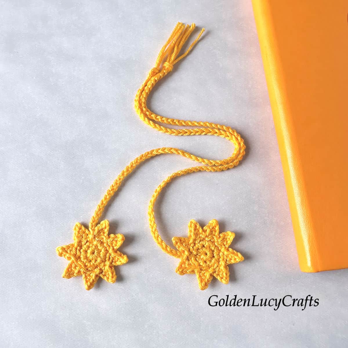 Two yellow crocheted sun bookmarks, placed next to an orange book.
