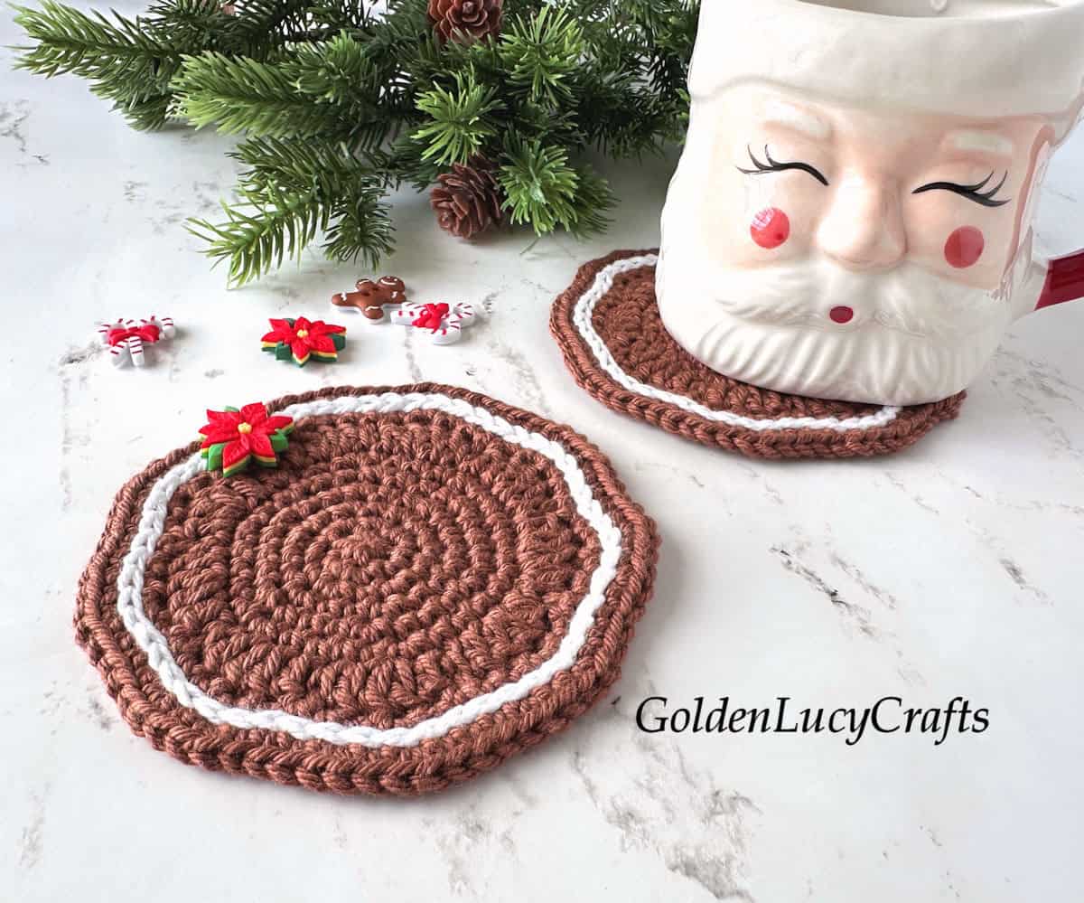 Two crocheted gingerbread-themed coasters in brown and white, embellished with Christmas decorative buttons; a Santa mug is on one of the coasters.