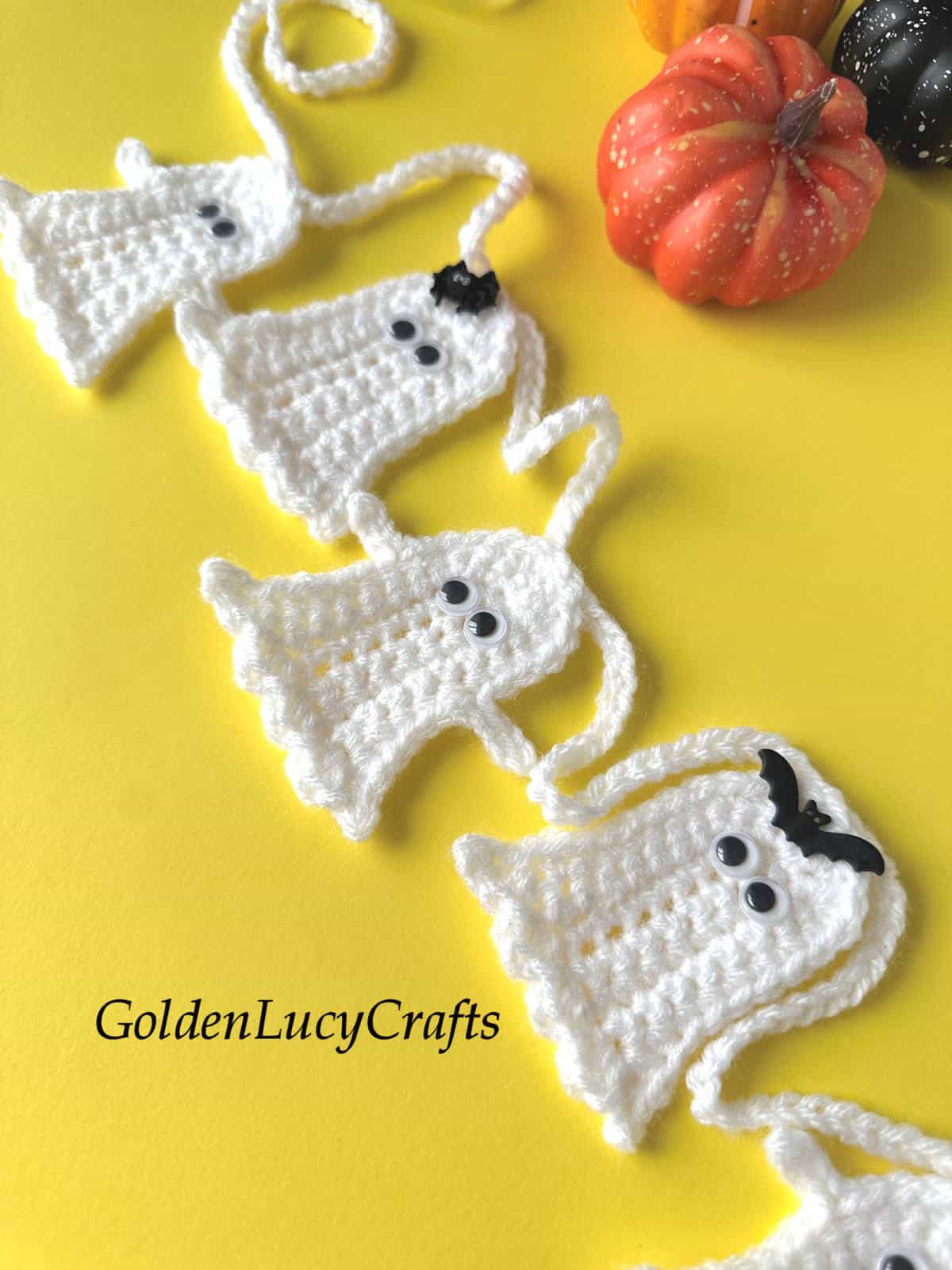 Close up picture of crocheted ghost garland on yellow background.